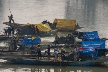Fishermen working on traditional boats gathering resources on a calm lake.